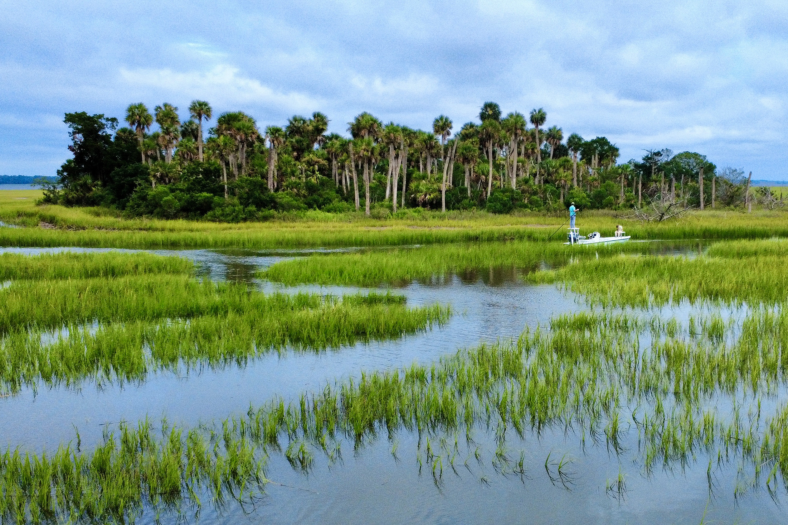 A fishing charter on shallow waters surrounded by lush greenery and palm trees in Beaufort, South Carolina, with two anglers on a boat.